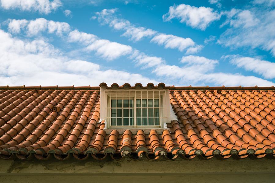 Toit de tuiles terracotta avec une lucarne à petits bois blancs, sous un ciel bleu