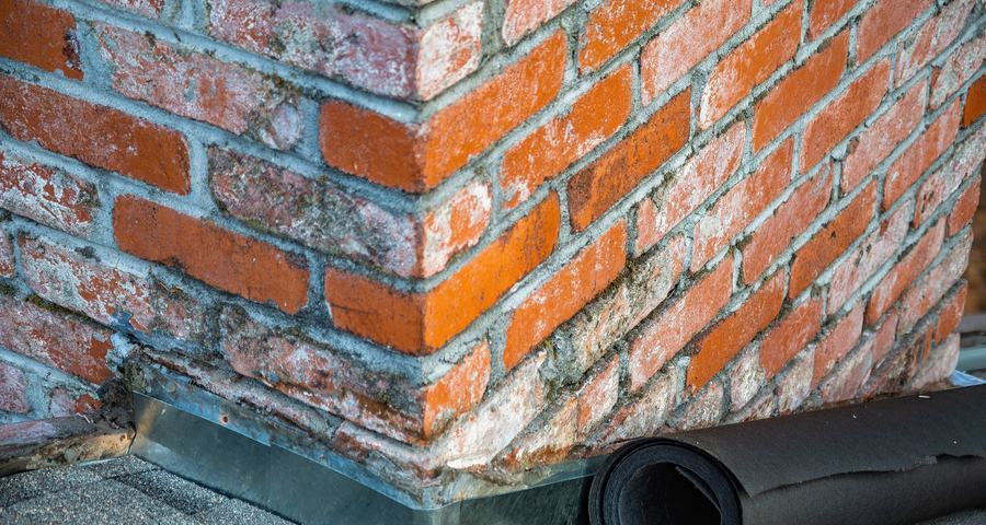 Angle d'une souche de cheminée en brique rouge, avec son solin en métal à la base